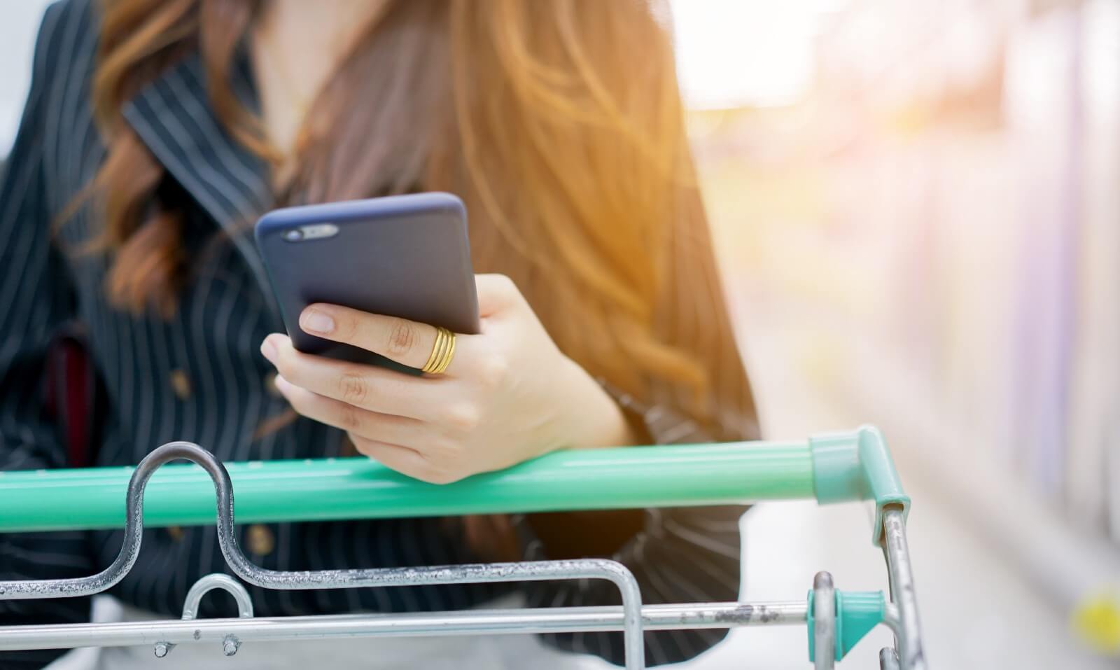 Woman pushing grocery cart while consulting phone