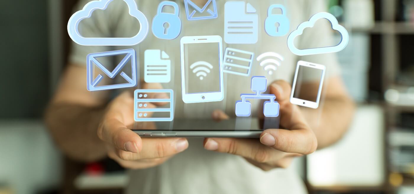 Blurry image of man shown from the shoulders down holding a tablet with various types of digital symbols overlaid — mobile, cloud, email, electronic documents, servers, and networks.