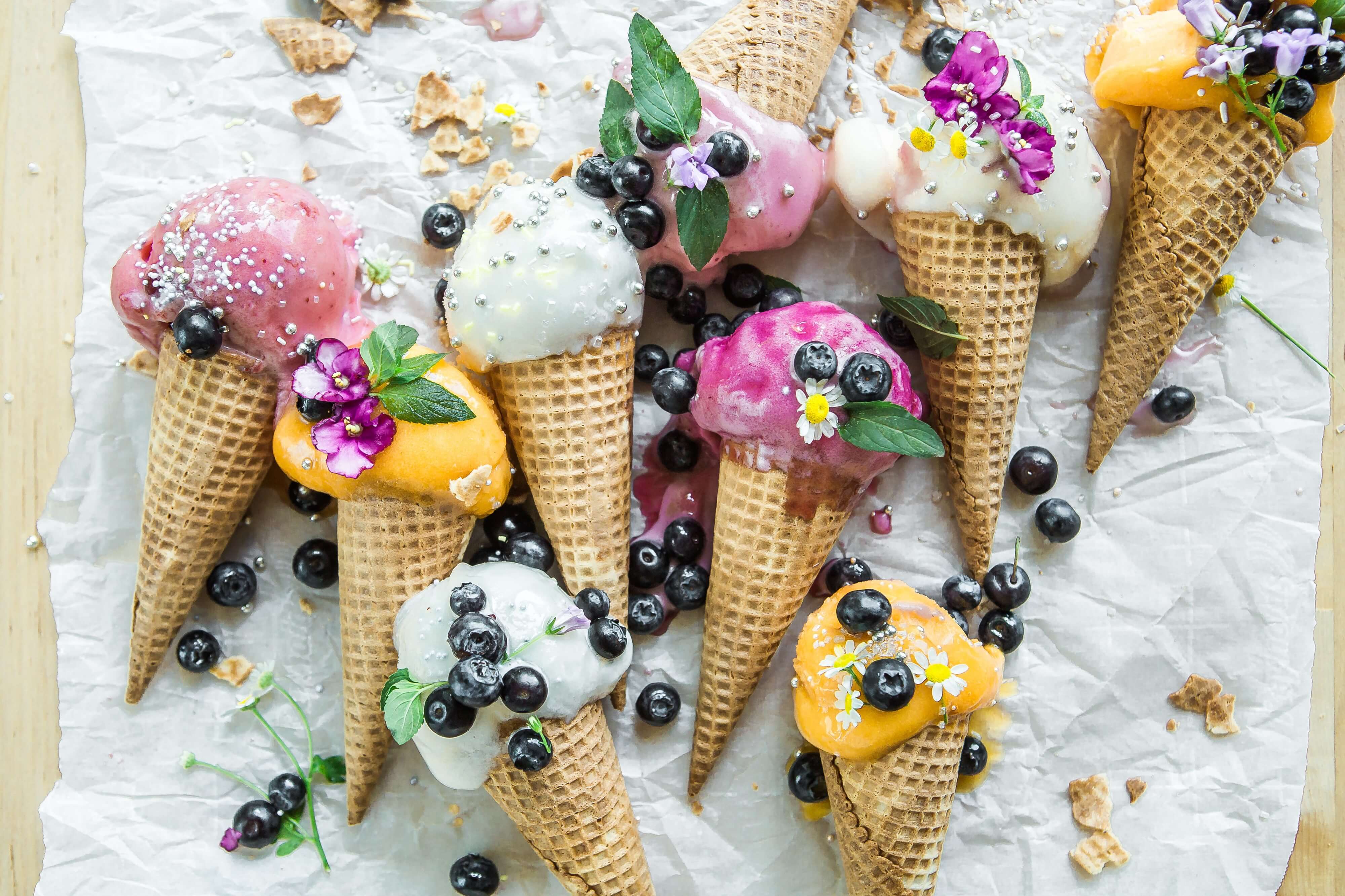 multiple ice cream cones with multiple flavors, colors and berries all around them