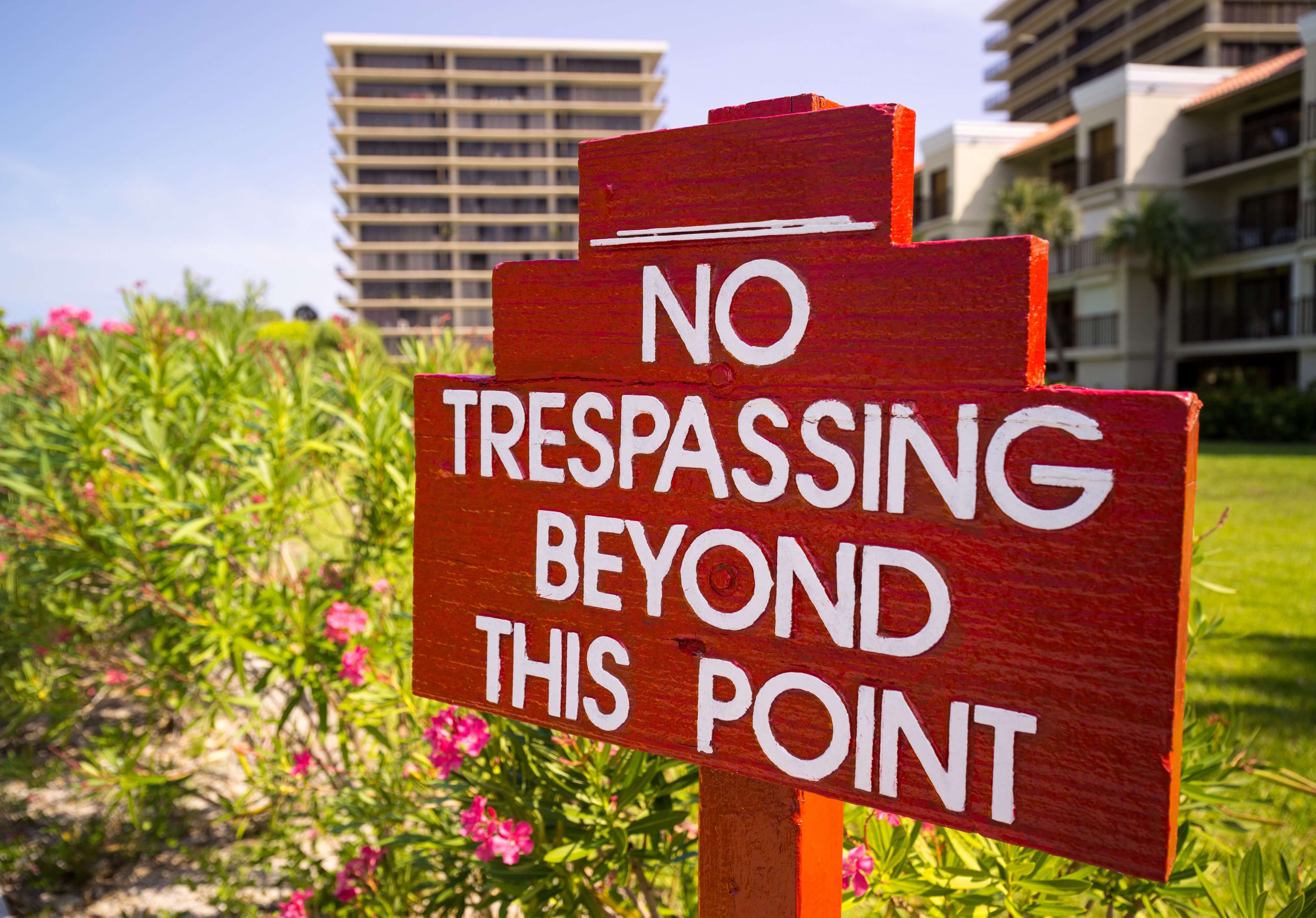 Red sign with white print on grass in front of tall buildings “no trespassing beyond this point