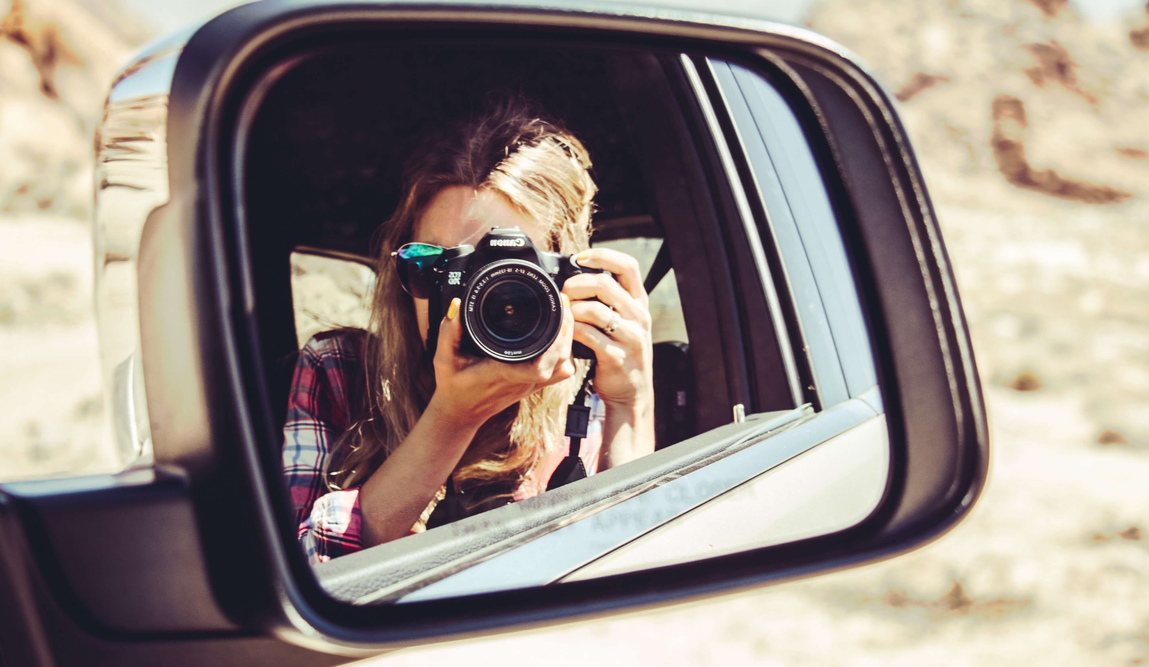 Woman taking photo reflected in car mirror
