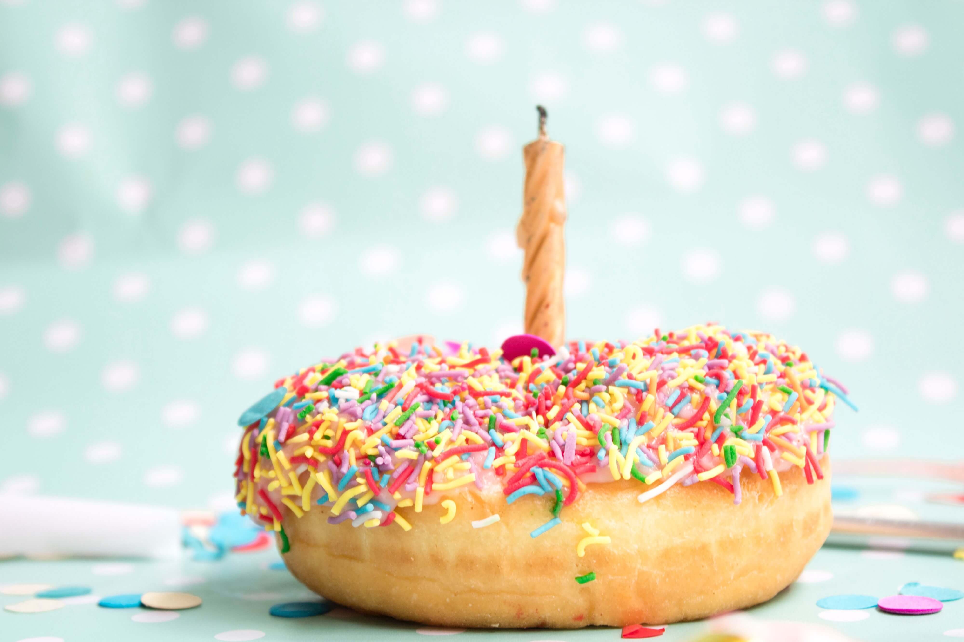 a colorful donut with one birthday candle on the top