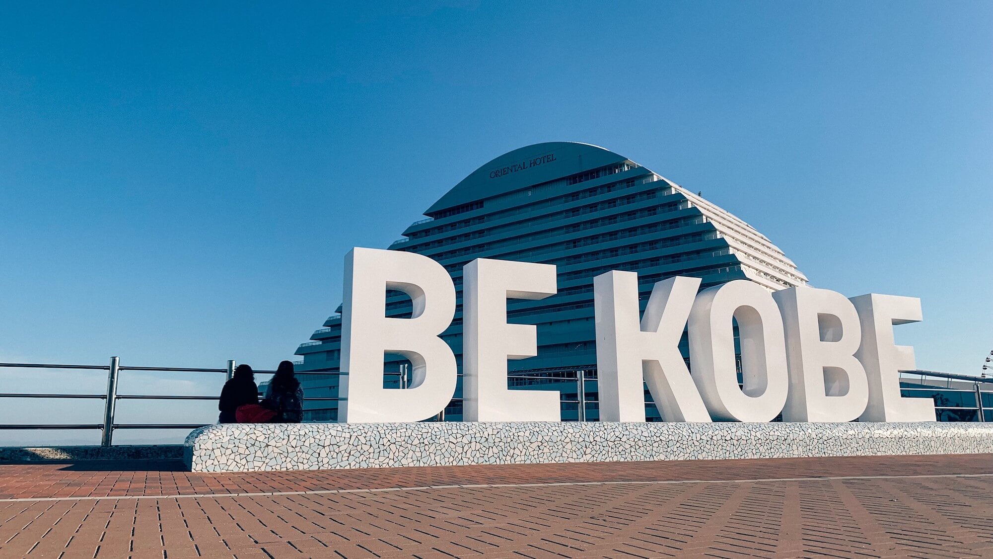 Large domed building with large white letters in front that say “Be Kobe”