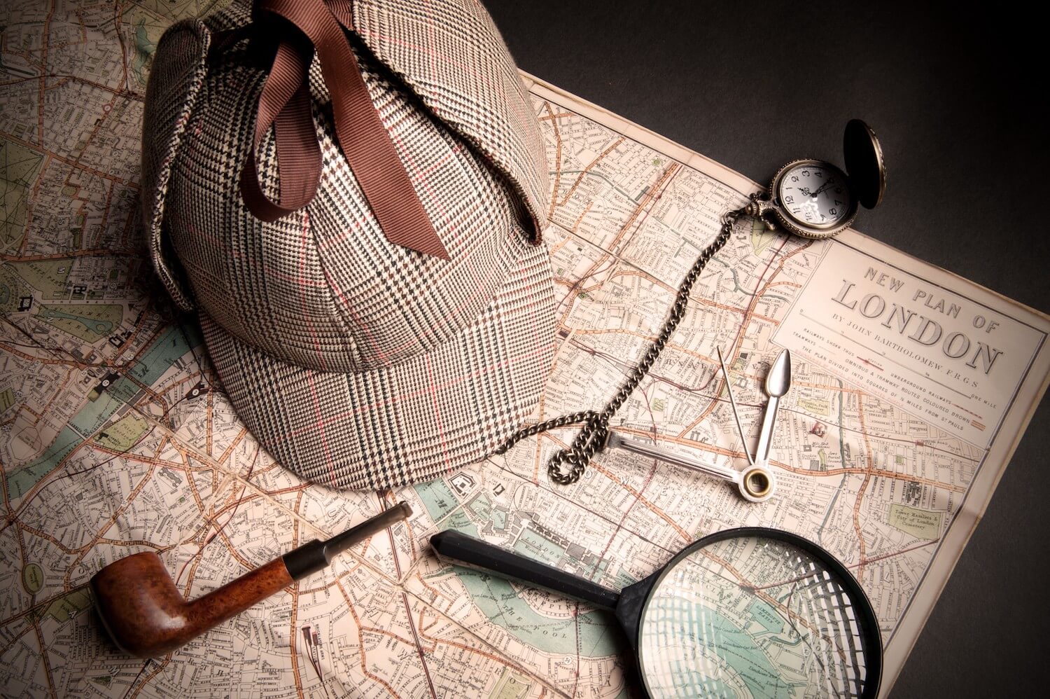 vintage detective hat, magnifying glass, pipe and vintage clock put on n old map