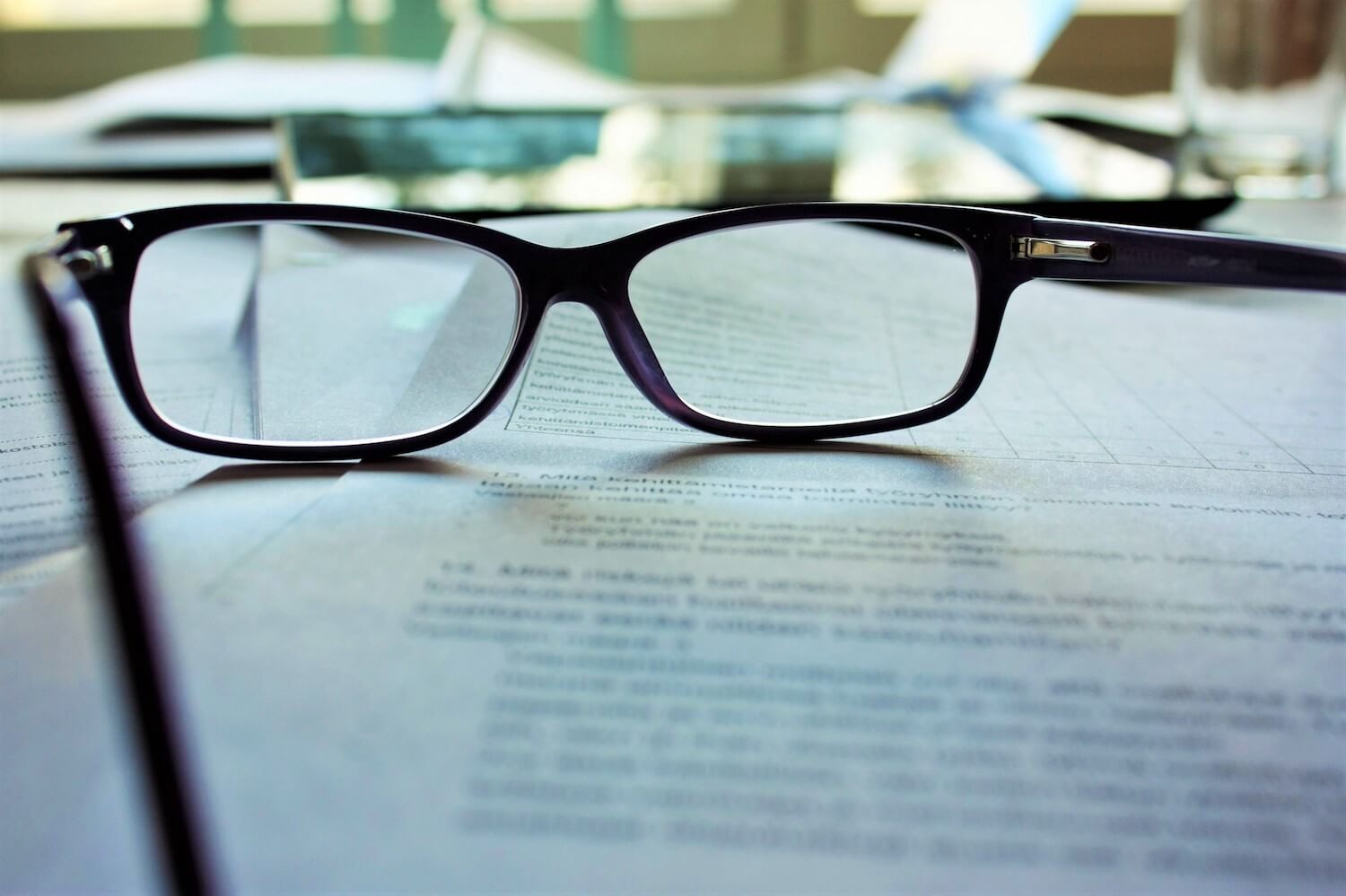 Black oval eye glasses on an out-of-focus stack of paper