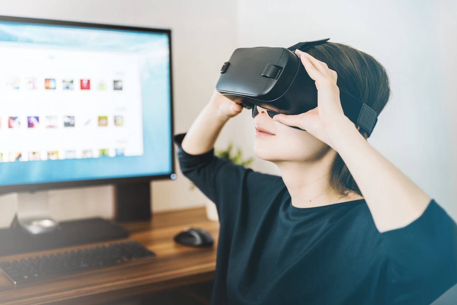 Woman in teal t-shirt sitting in front of large monitor wearing VR goggles