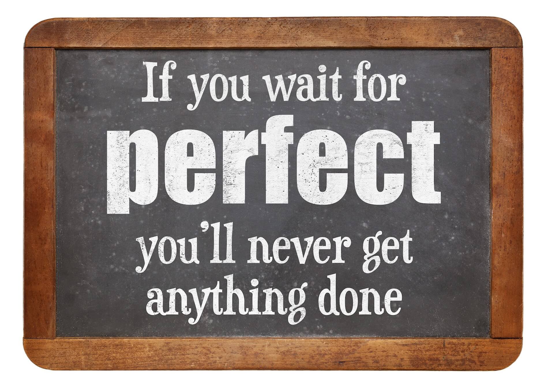 Blackboard with wooden rim with “If you wait for perfect, you’ll never get anything done” written in white chalk