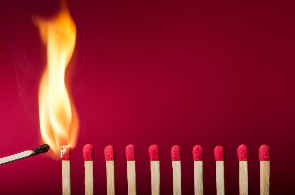 Row of closely spaced unlit wooden matches next to two that are burning against a red background
