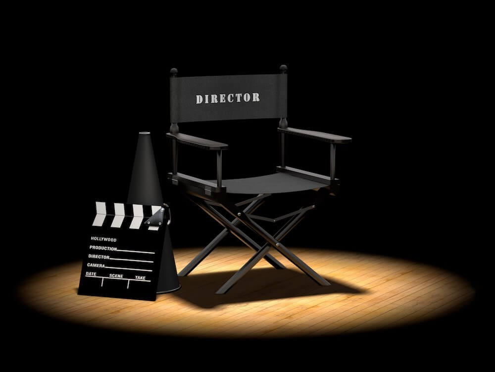 Black directors chair, camera slate, and megaphone in a spotlight on a wooden floor