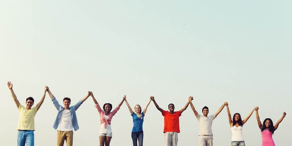 Eight people of different races and genders holding hands up in the air